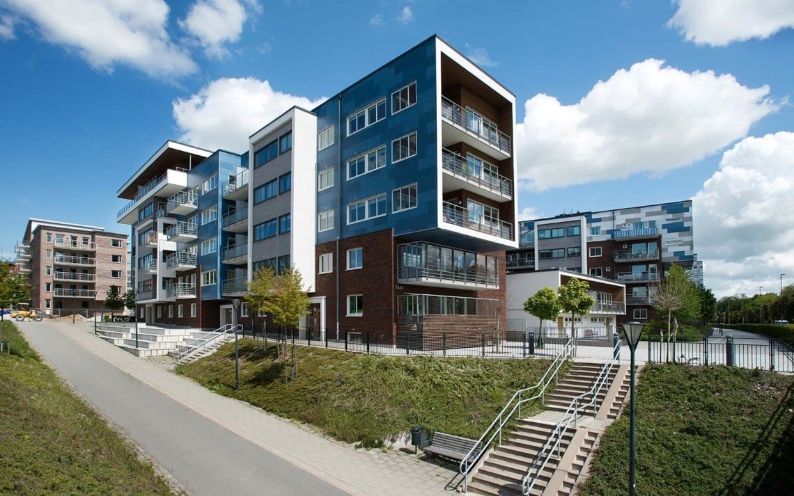En modern bostadsbyggnad med flera våningar och en blandning av blå, vit och tegelröd fasad. Varje 